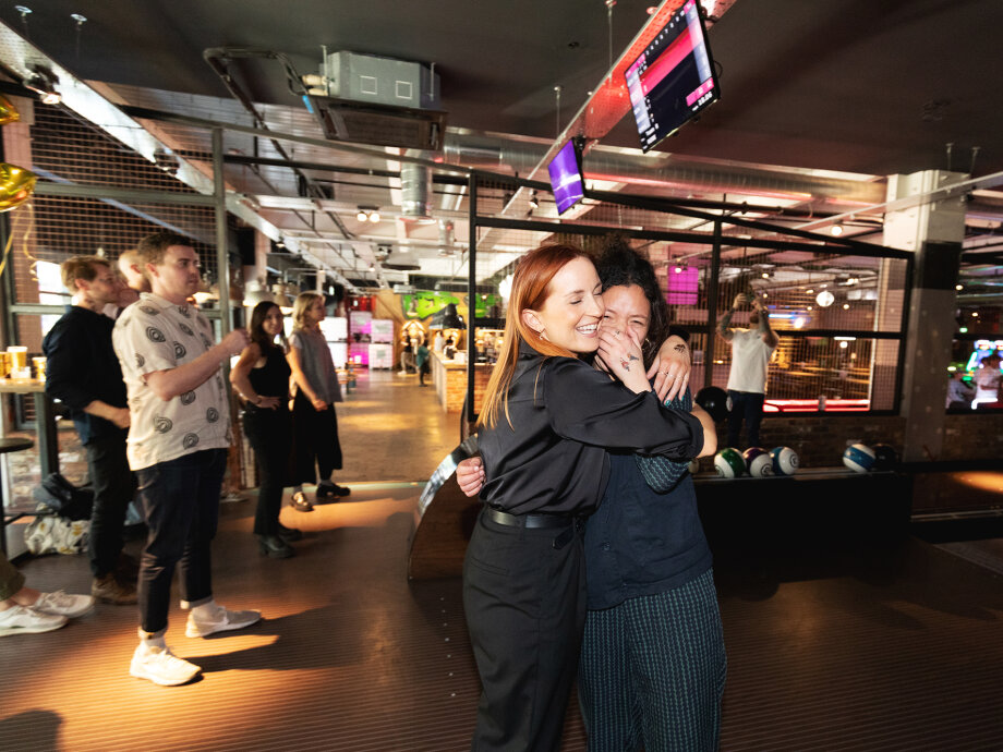 Fiasco Design turns 13! Photo shows 2 people hugging at a bowling alley.