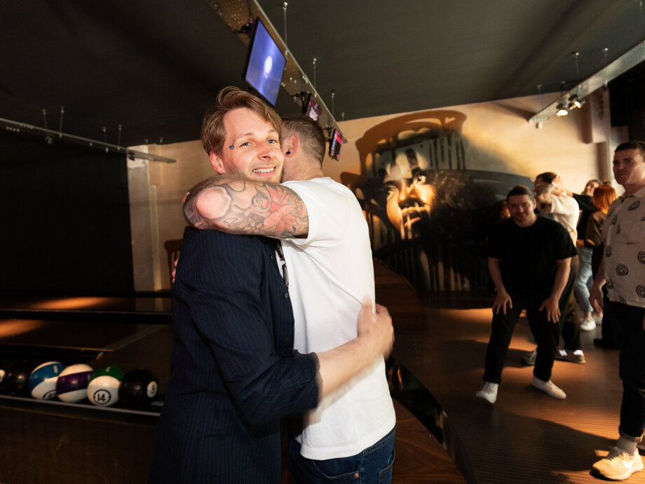 Fiasco Design turns 13! Photo shows 2 men hugging at bowling alley.